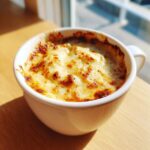Close-up of warm, bubbly beer cheese dip topped with golden-brown melted cheese in a white mug.