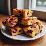 Stack of golden brown, square slices of berry sheet pan pancakes with visible red fruit pieces.