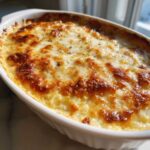 Close-up of a hot, creamy popper dip baked in a white dish with a bubbly, golden-brown cheese topping.