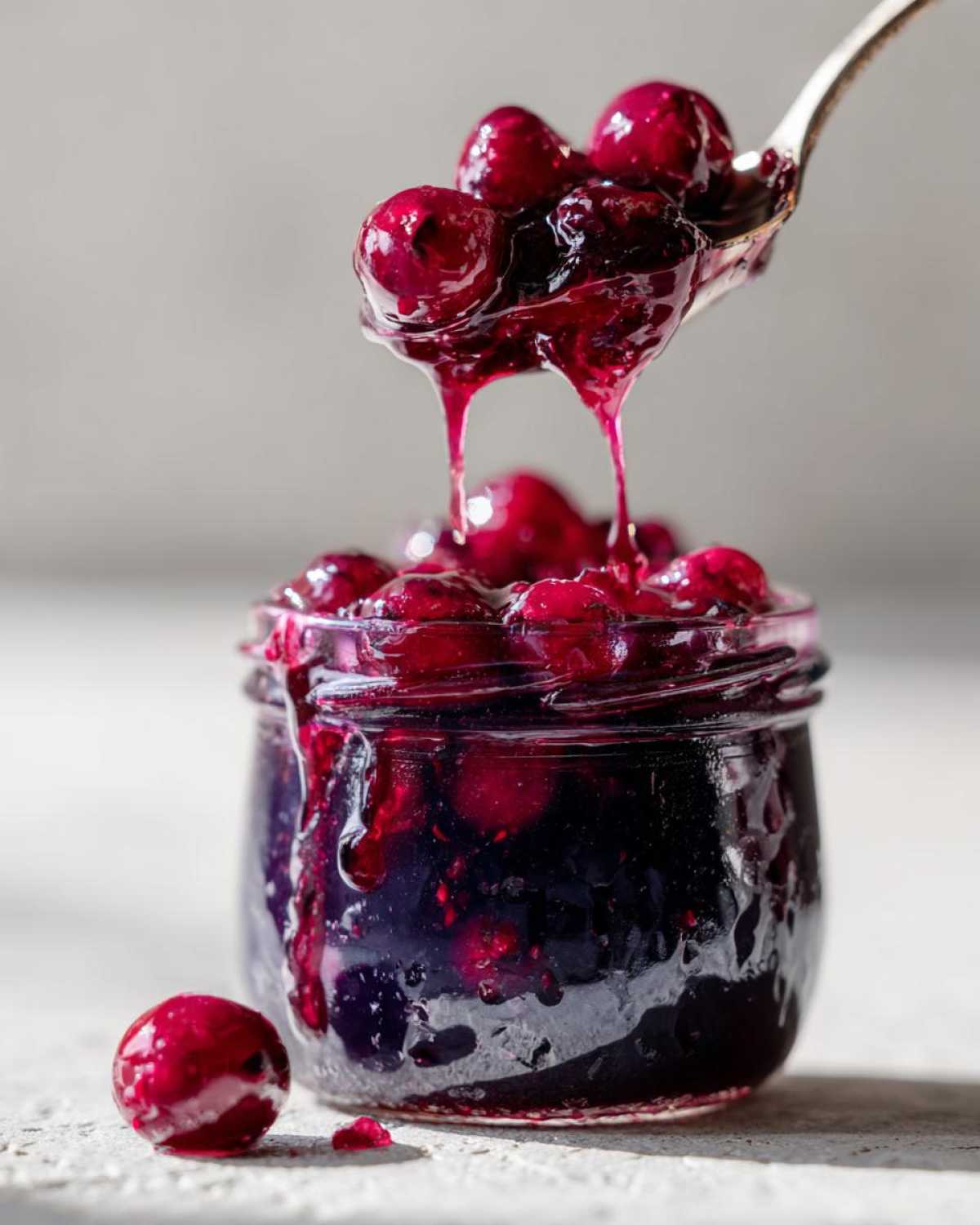 A spoonful of thick, whole-fruit blueberry jam dripping back into a small jar of homemade blueberry jam.