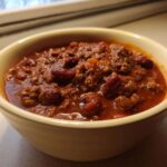 Close-up of a creamy yellow bowl filled with rich, thick best chili recipe featuring ground beef and kidney beans.
