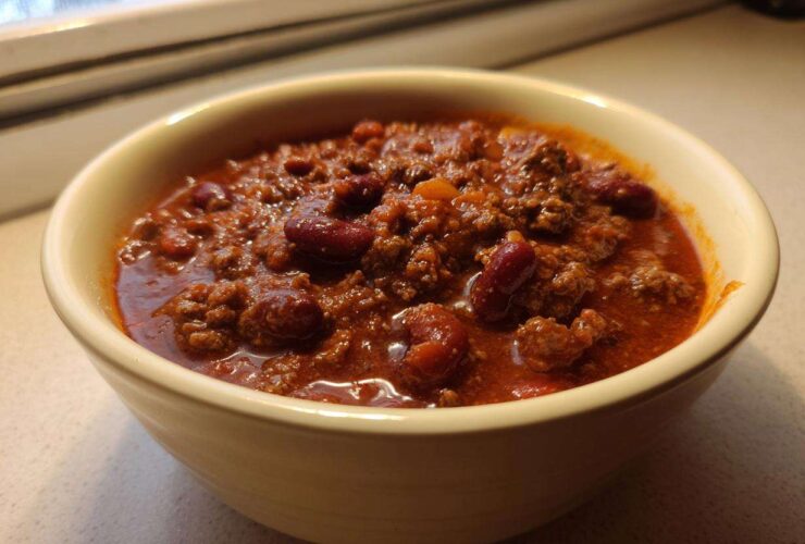 Close-up of a creamy yellow bowl filled with rich, thick best chili recipe featuring ground beef and kidney beans.