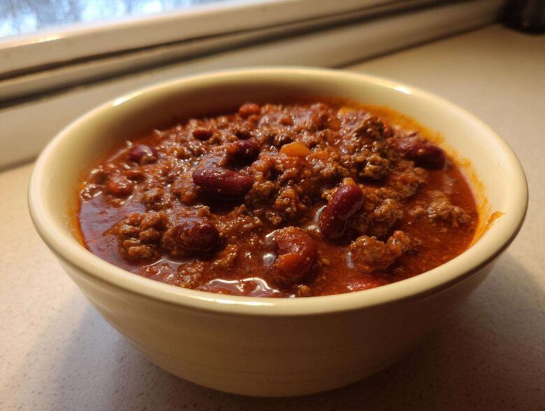Close-up of a creamy yellow bowl filled with rich, thick best chili recipe featuring ground beef and kidney beans.