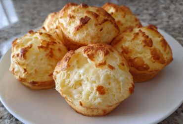 A close-up of several golden-brown Brazilian cheese bread puffs piled on a white plate.