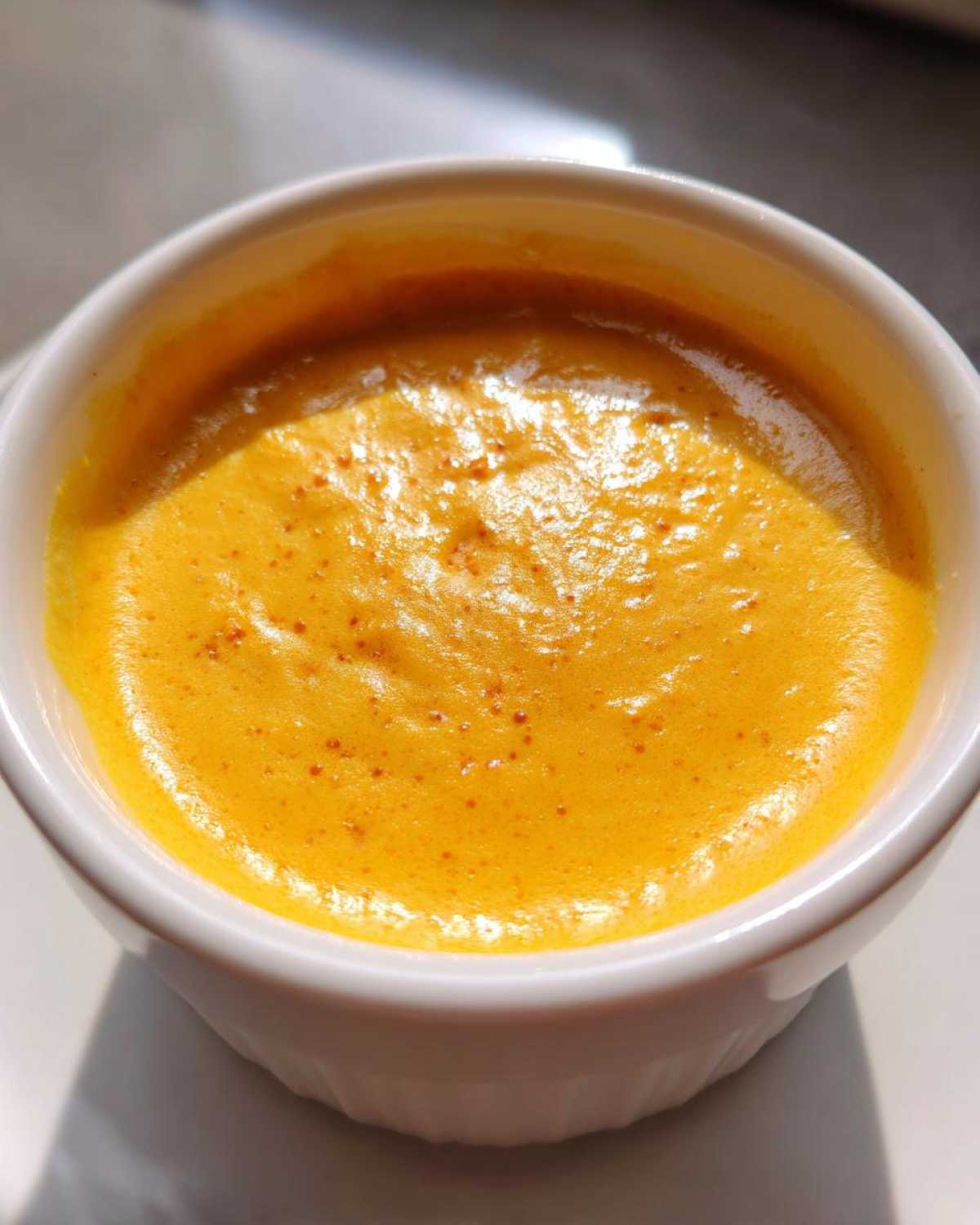 Close-up of bright orange, smooth beer cheese dip with small bubbles in a white ramekin.