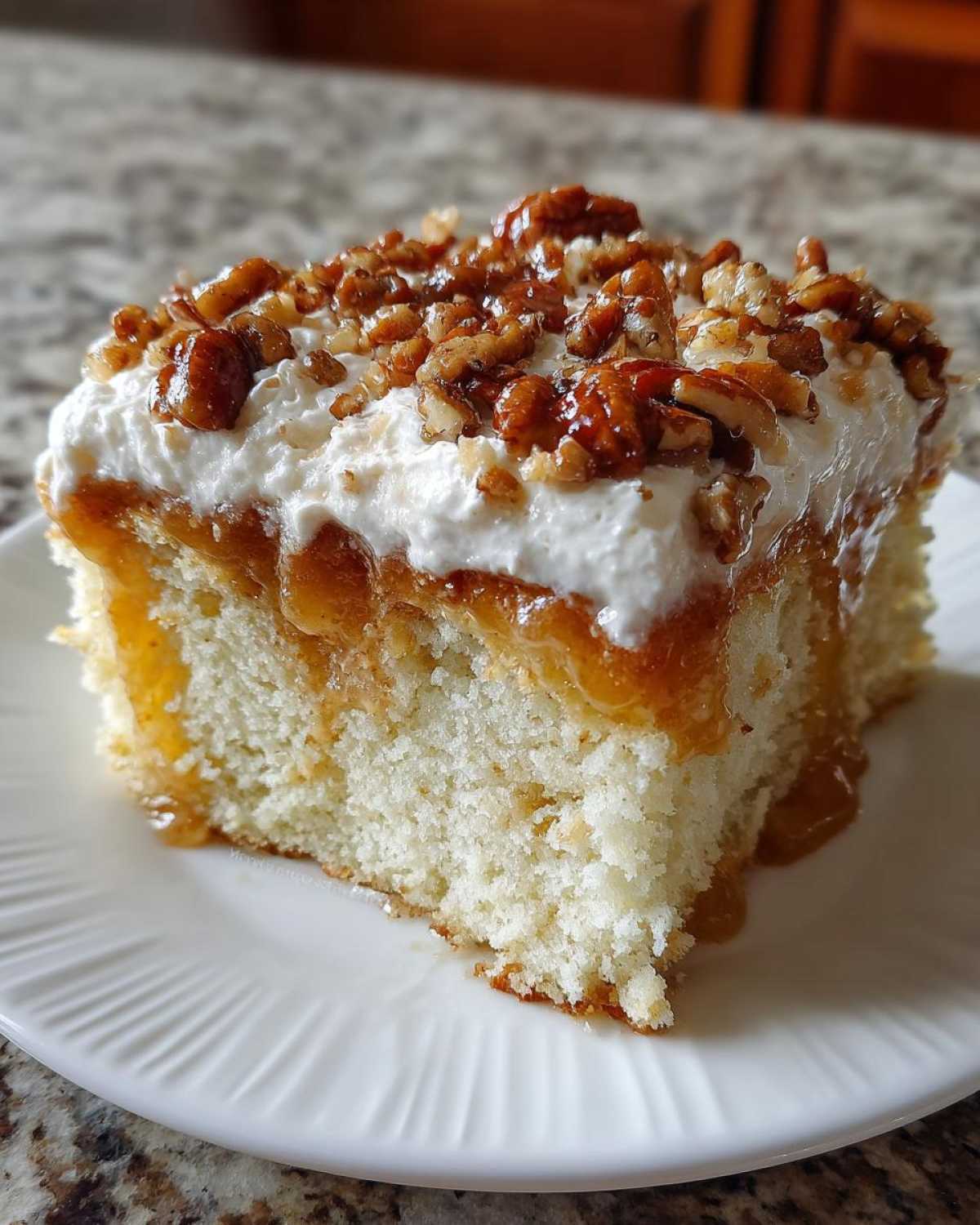 A close-up of a moist slice of butter pecan praline poke cake topped with whipped cream and candied pecans.