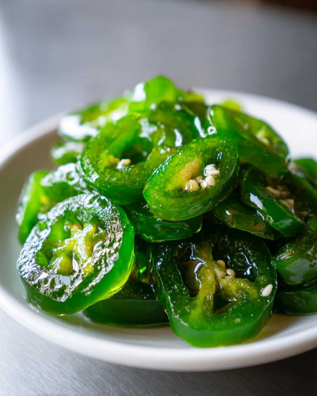 Close-up of glossy, bright green slices of candied jalapenos piled on a small white plate.