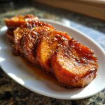 Four thick slices of glistening candied sweet potatoes covered in a rich, dark brown glaze, served on a white plate.