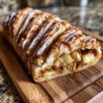 A close-up of a freshly baked apple strudel filled with spiced apples, drizzled with caramel and icing.