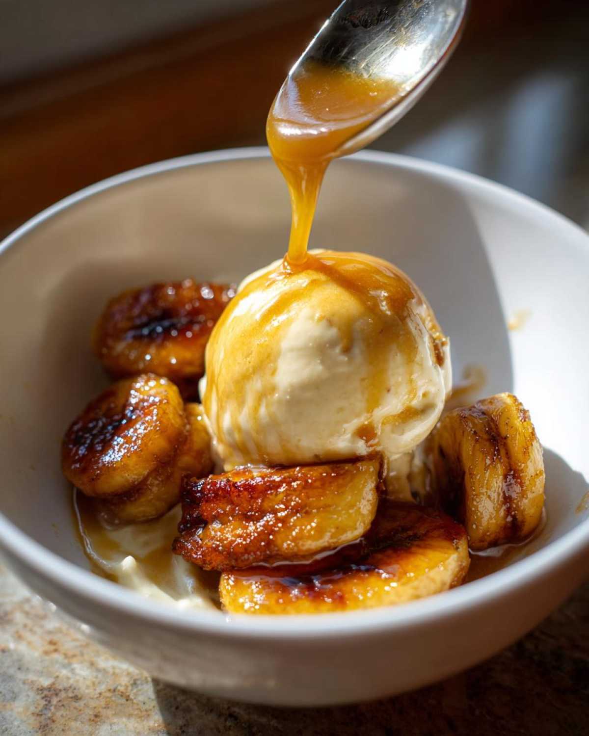 A spoonful of caramel sauce is drizzled over a scoop of vanilla ice cream and caramelized bananas, the perfect Bananas Foster dessert.