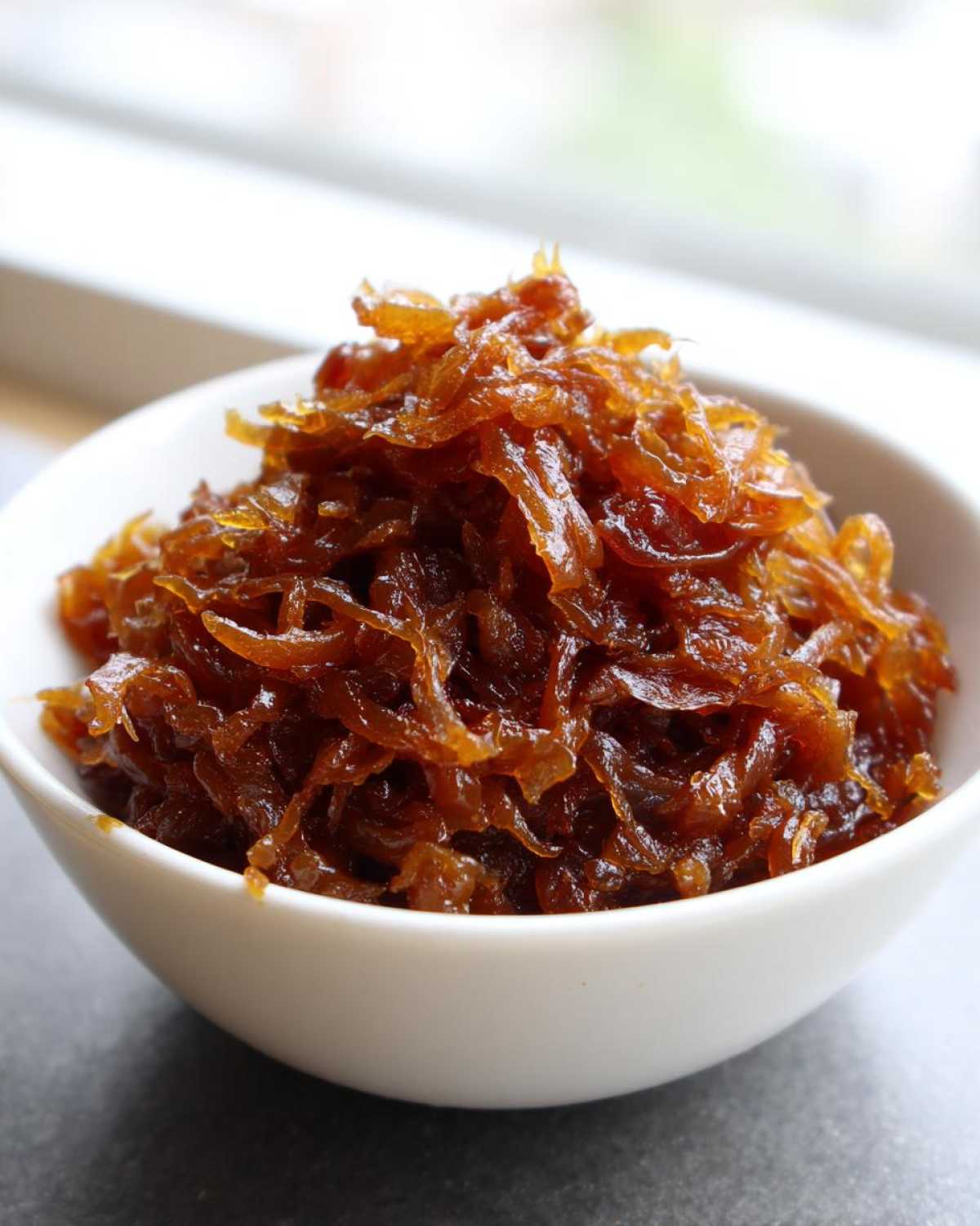 A close-up of deeply brown, glossy caramelized onions piled high in a small white bowl.