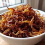 Close-up of deeply browned and glossy caramelized onions piled high in a small white bowl.