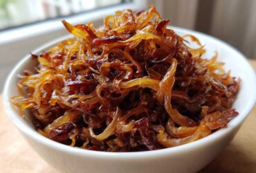 Close-up of deeply browned and glossy caramelized onions piled high in a small white bowl.