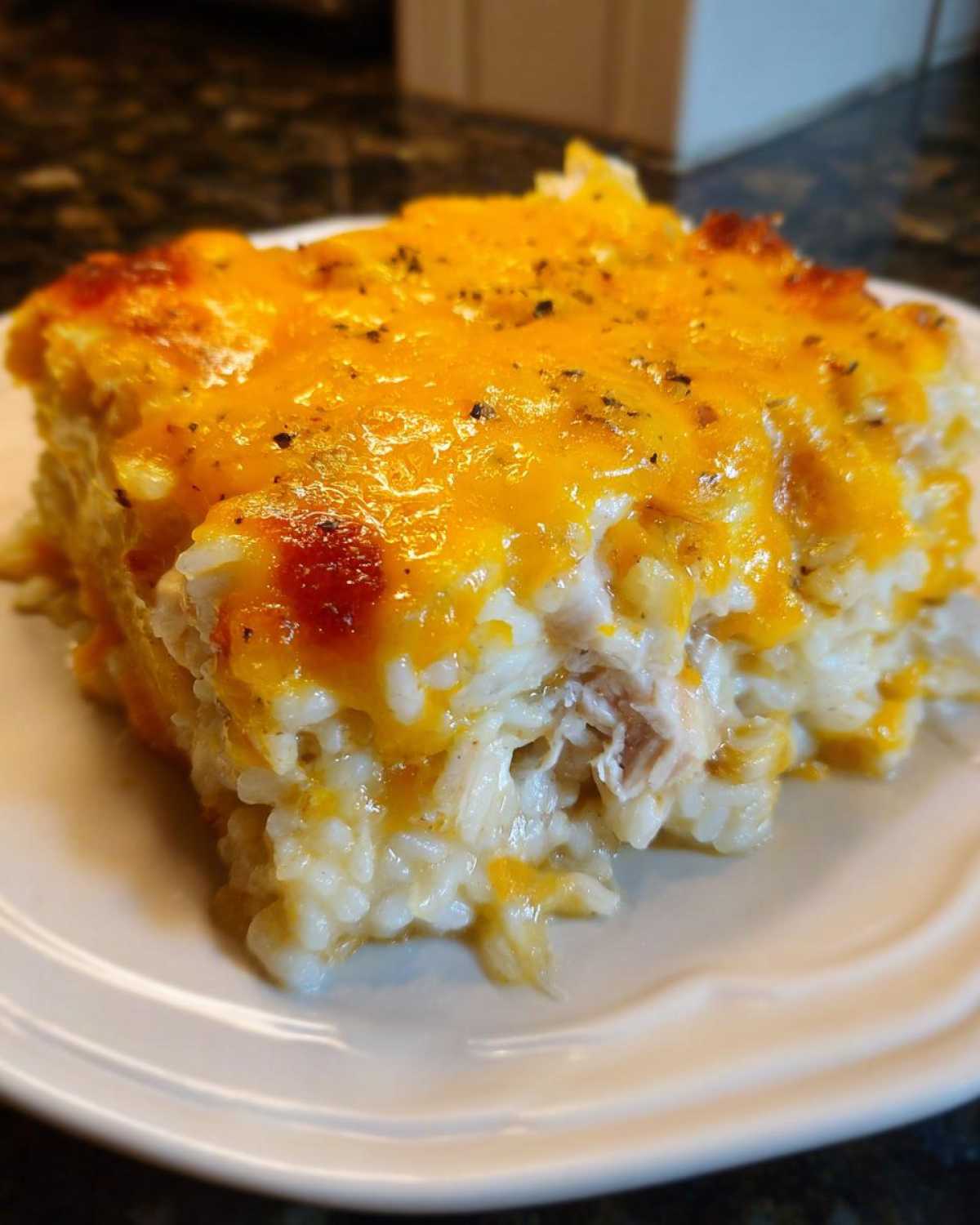 Close-up of a serving of creamy chicken and rice casserole topped with melted cheddar cheese and herbs.