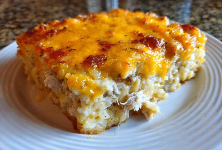 A close-up of a hearty slice of chicken and rice casserole topped with melted, browned cheddar cheese.