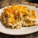 A close-up serving of creamy, shredded cheesy chicken and rice topped with melted, slightly browned cheddar cheese.