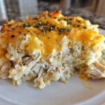 Close-up of a portion of cheesy chicken and rice casserole topped with melted cheddar and herbs.