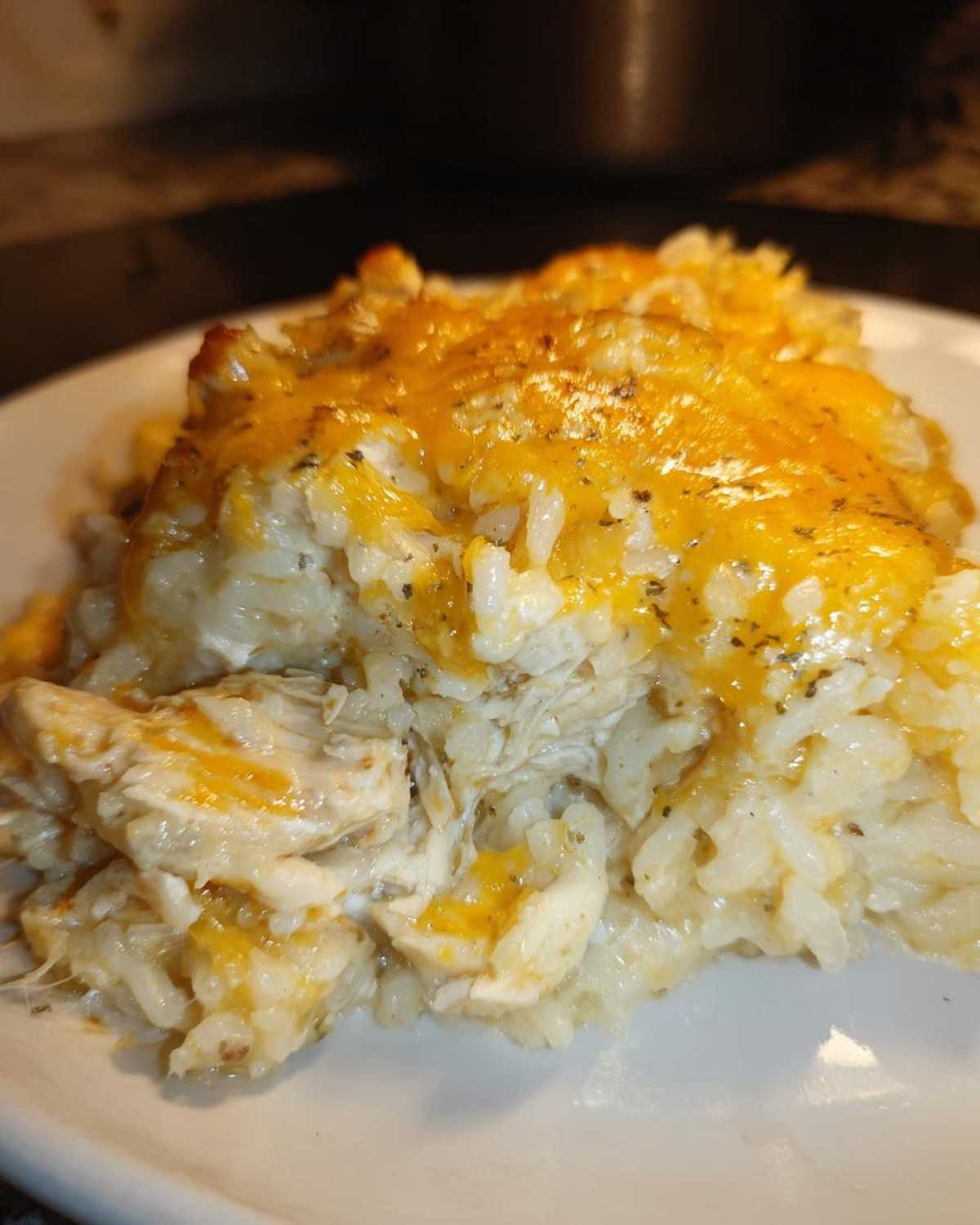 Close-up of a scoop of creamy cheesy chicken and rice casserole topped with melted cheddar cheese.