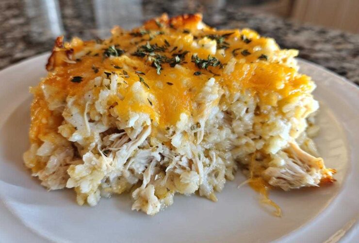 Close-up of a portion of cheesy chicken and rice casserole topped with melted cheddar and herbs.
