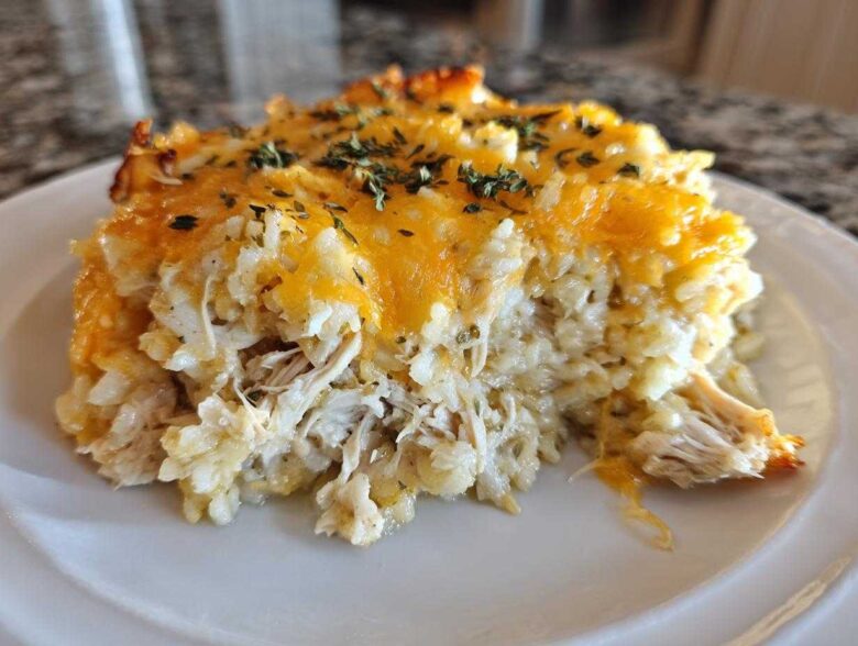 Close-up of a portion of cheesy chicken and rice casserole topped with melted cheddar and herbs.