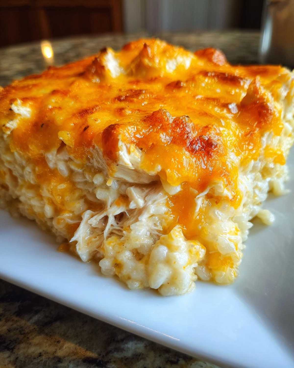 A close-up of a square serving of cheesy chicken and rice, topped with melted, browned cheddar cheese.