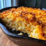 A close-up view of a creamy, cheesy hashbrown casserole baked in a black cast iron skillet, showing a crispy, golden-brown topping.