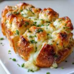 Close-up of baked hawaiian roll garlic bread, melted cheese oozing out, topped with fresh green parsley.