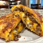 Close-up of garbage bread cut in half, showing melted cheese and ground meat filling oozing out.