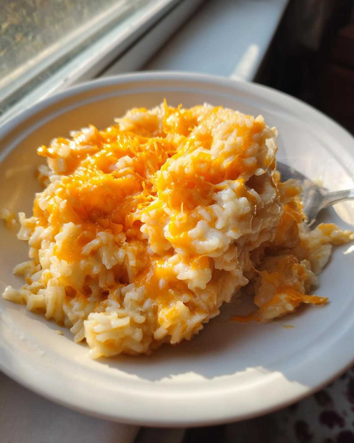 A close-up serving of creamy, warm cheesy rice topped with melted orange cheddar cheese.