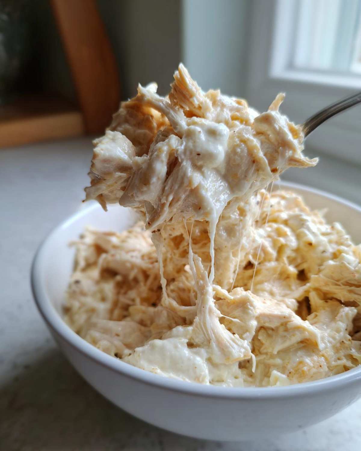 A spoonful of creamy, cheesy shredded chicken being lifted from a bowl of crockpot white chicken chili.