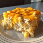 A square serving of creamy chicken and rice casserole topped with melted cheddar cheese.