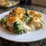 A close-up serving of Chicken Divan casserole featuring creamy sauce, chicken pieces, and bright green broccoli topped with melted cheddar cheese.