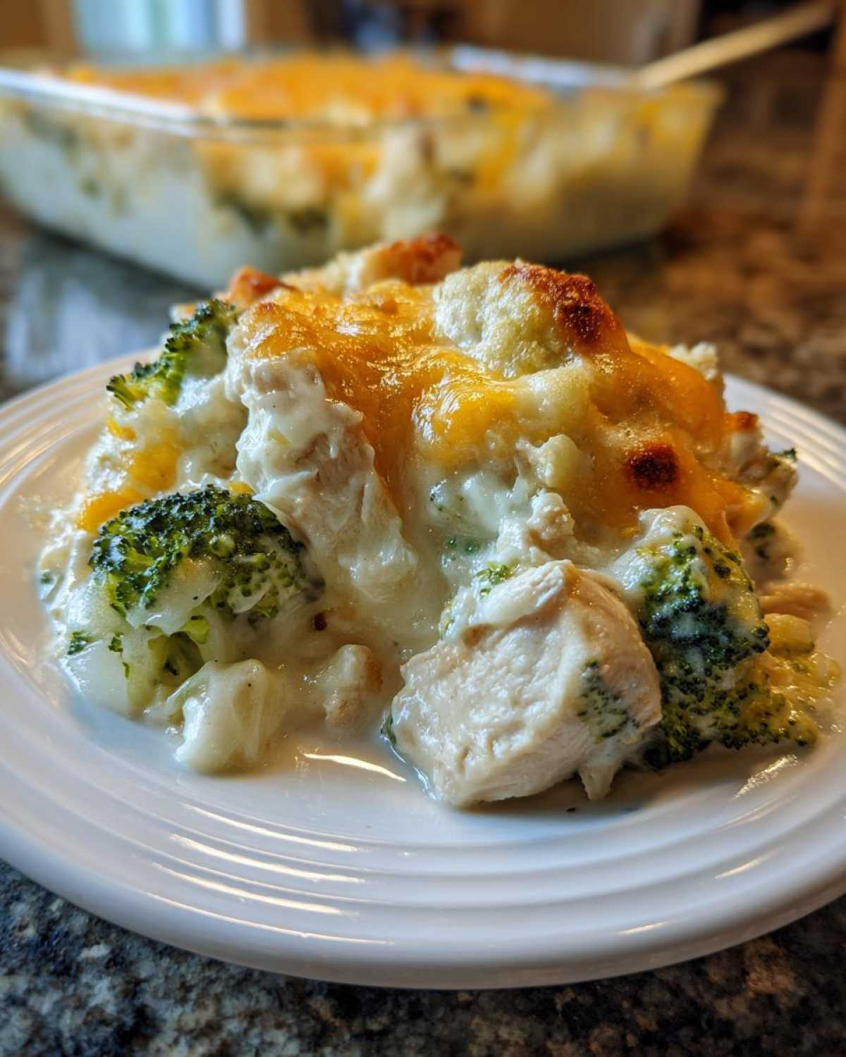 A close-up serving of creamy Chicken Divan casserole featuring chunks of chicken and bright green broccoli topped with melted, browned cheese.