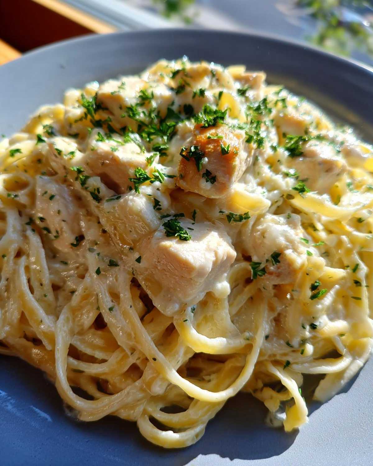 Close-up of a plate of rich chicken fettuccine alfredo pasta topped with chopped fresh parsley.