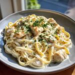 A close-up of rich chicken fettuccine alfredo pasta coated in creamy sauce and topped with fresh parsley.