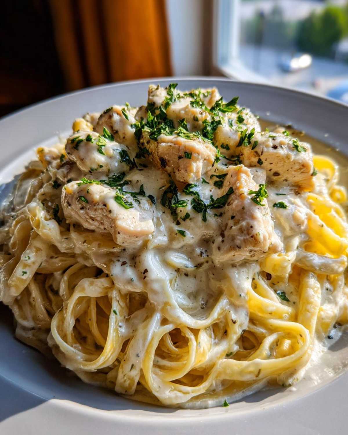 Close-up of rich chicken fettuccine alfredo pasta generously coated in white sauce and topped with diced chicken and fresh parsley.