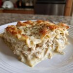Close-up of a generous slice of 8-layer chicken lasagna with shredded chicken and melted cheese topping.