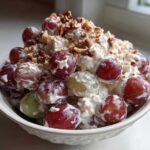 A white bowl filled with creamy chicken salad chick grape salad, topped with chopped pecans.