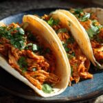 Three soft corn tortillas filled with saucy shredded chicken tinga and topped with fresh cilantro.