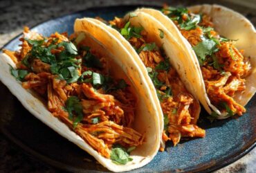 Three soft corn tortillas filled with saucy shredded chicken tinga and topped with fresh cilantro.