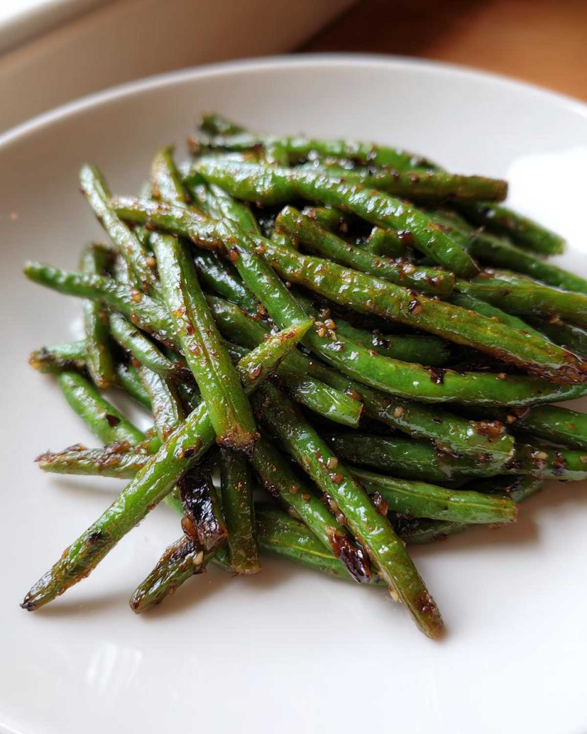 A serving of glossy, blistered chinese green beans with garlic sauce piled on a white plate.