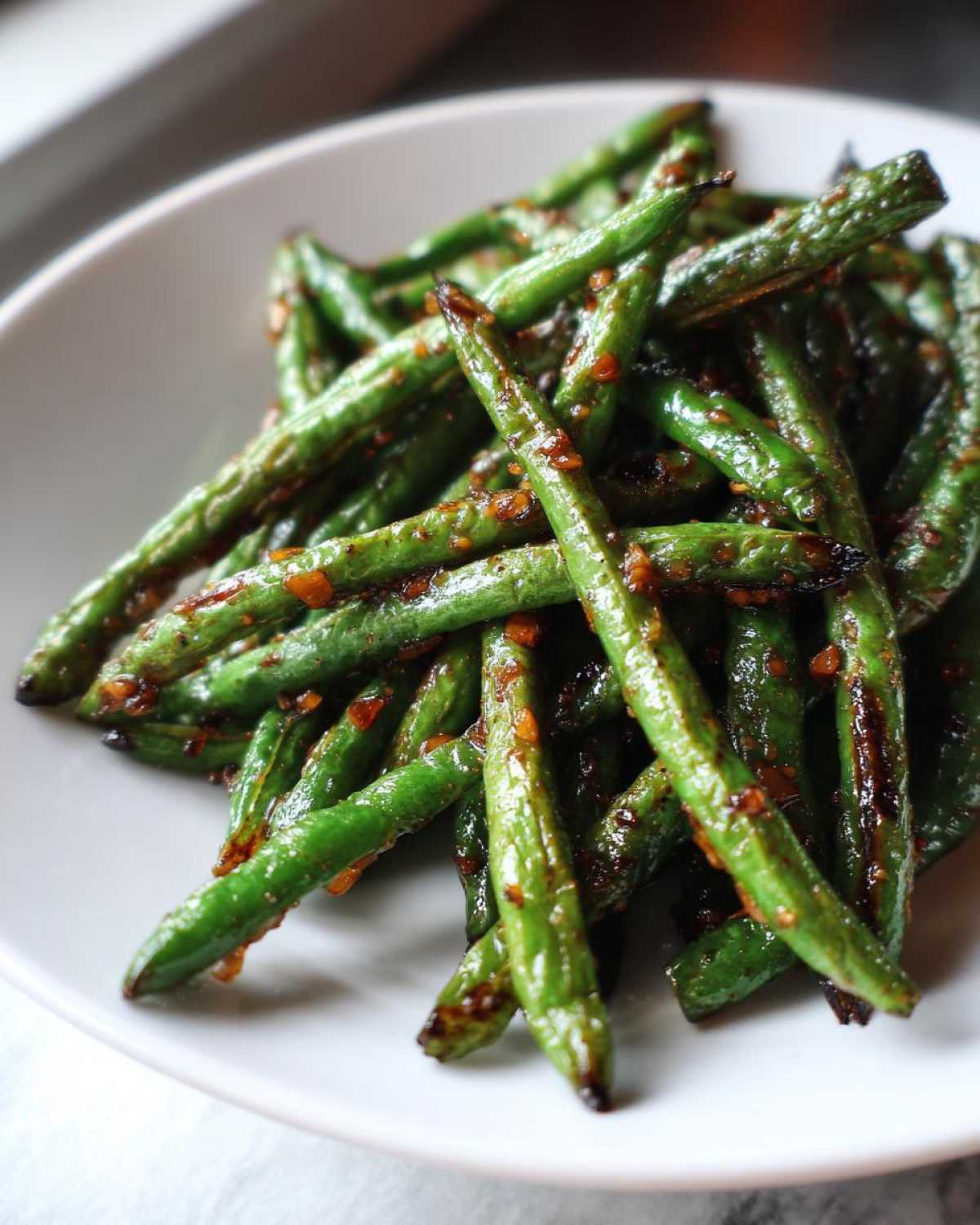 Close-up of blistered chinese green beans with garlic sauce served in a white bowl.