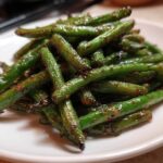 A pile of glossy, stir-fried chinese green beans with garlic sauce served on a white plate.
