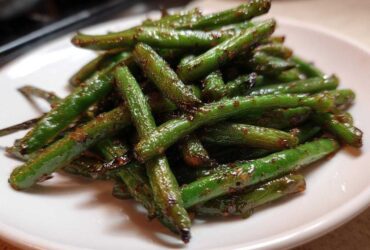 A pile of glossy, stir-fried chinese green beans with garlic sauce served on a white plate.