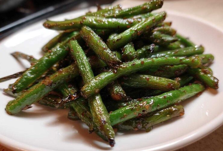 A pile of glossy, stir-fried chinese green beans with garlic sauce served on a white plate.