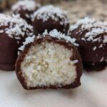 Close-up of chocolate-dipped coconut balls, one cut open showing the shredded white coconut filling of the coconut balls.