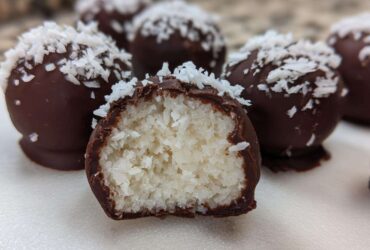 Close-up of chocolate-dipped coconut balls, one cut open showing the shredded white coconut filling of the coconut balls.