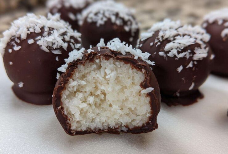 Close-up of chocolate-dipped coconut balls, one cut open showing the shredded white coconut filling of the coconut balls.