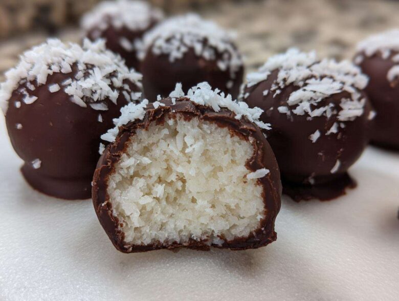 Close-up of chocolate-dipped coconut balls, one cut open showing the shredded white coconut filling of the coconut balls.