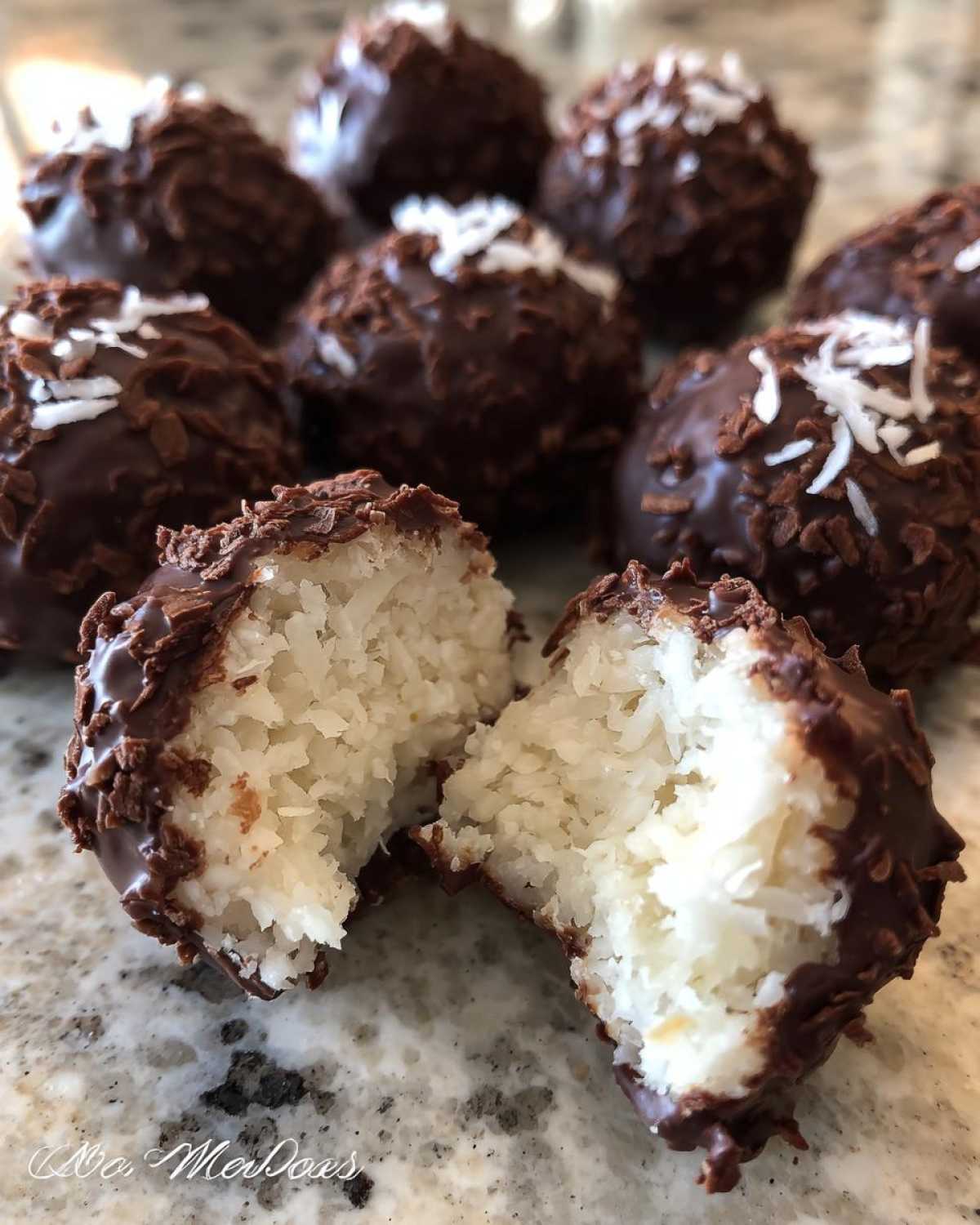 A chocolate-dipped coconut ball is broken in half, showing the white, shredded coconut interior of these amazing coconut balls.